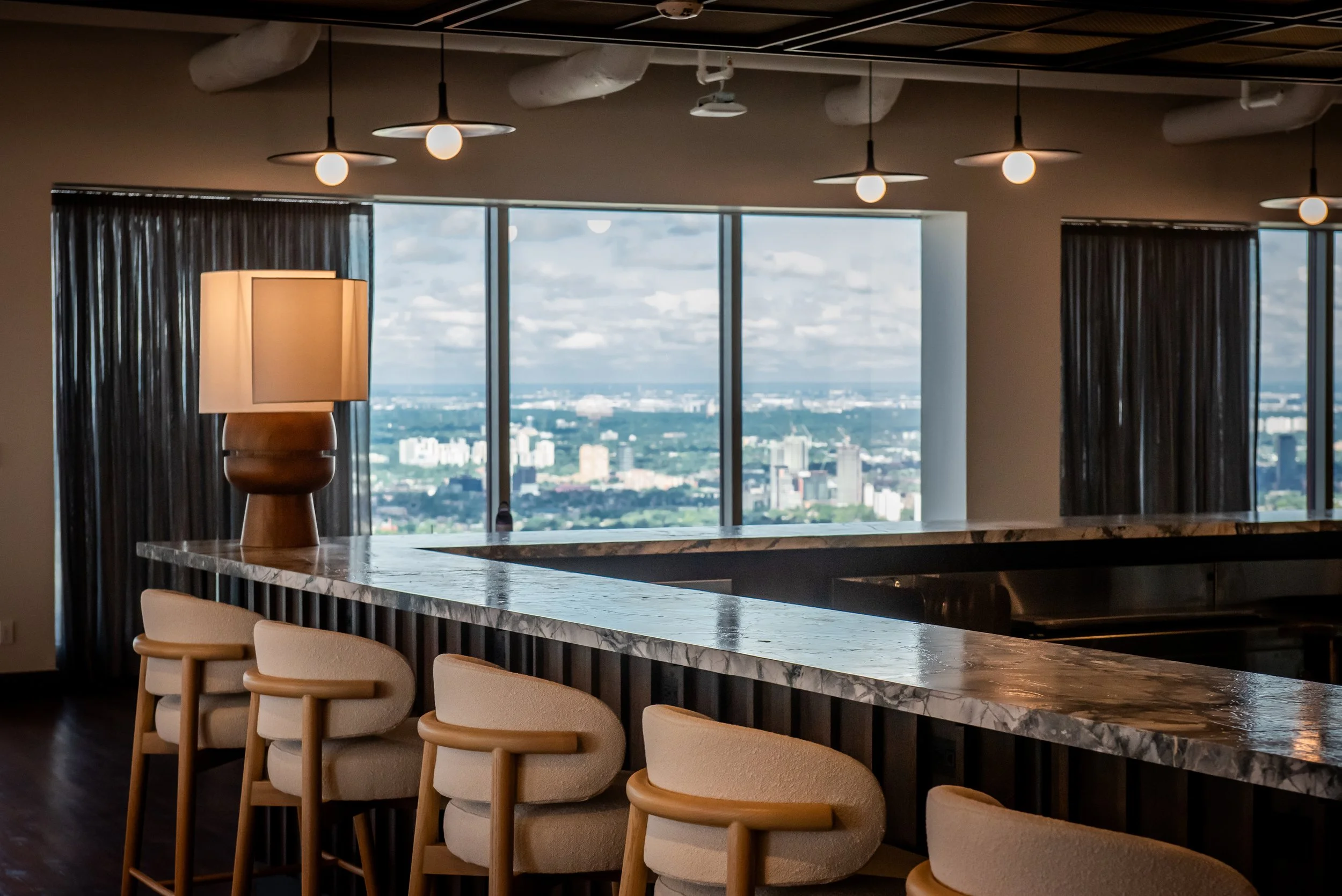 Large wood and stone bar with upholstered stools, warm lighting and Toronto views