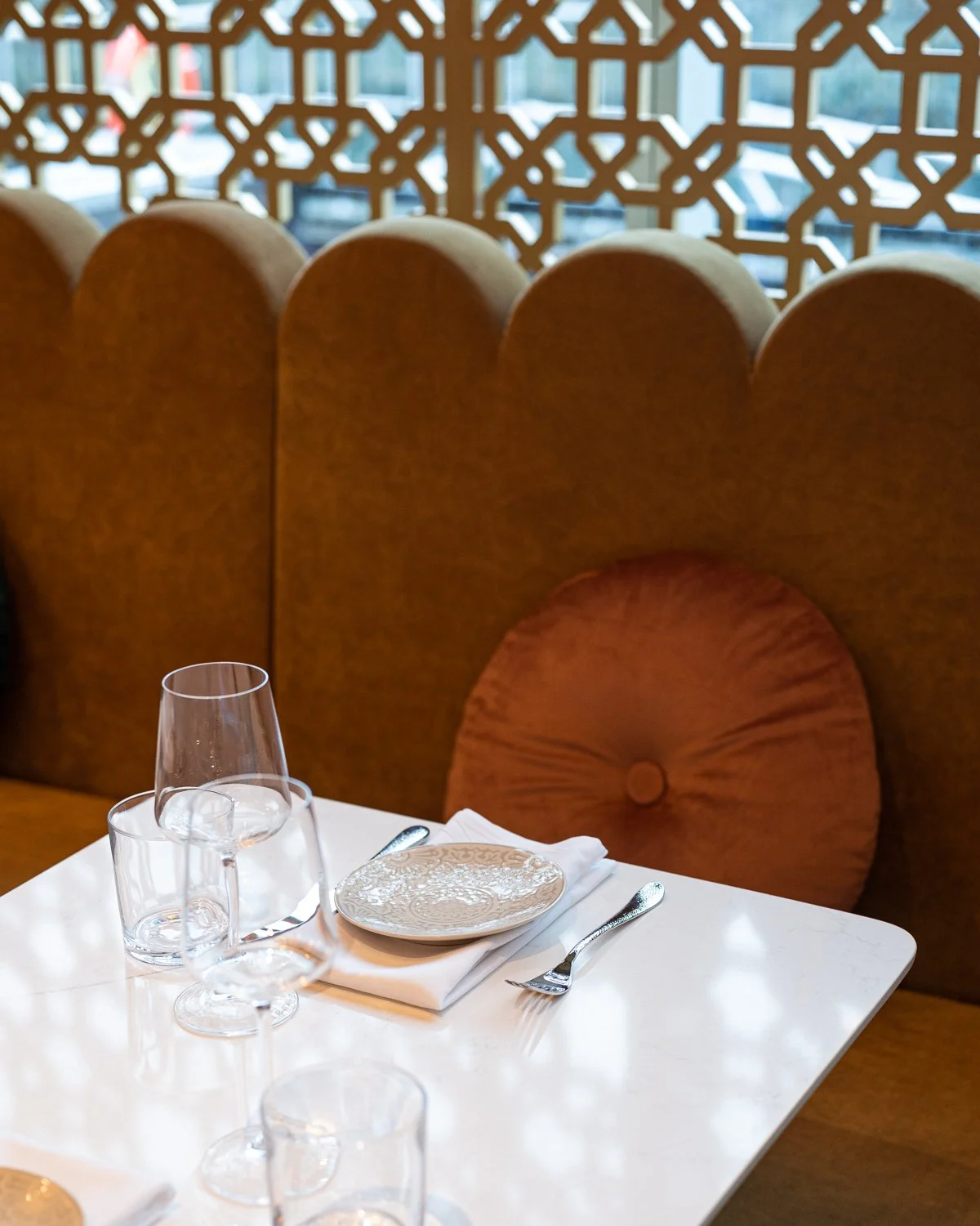 Restaurant white quartz table top with yellow scalloped top banquette and lattice screen beyond