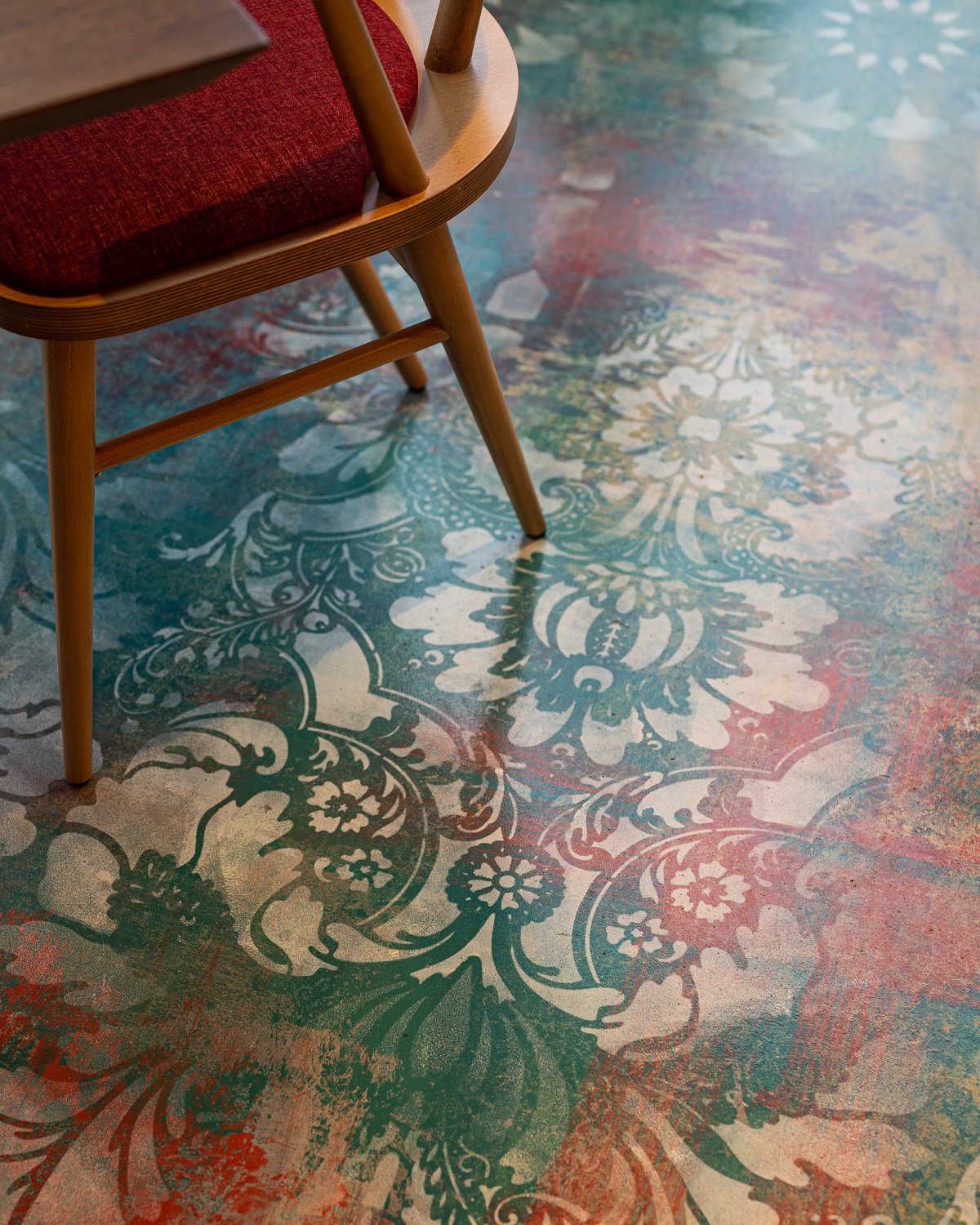Restaurant close up of floral painted patterned floor with wood chair and red seat cushion
