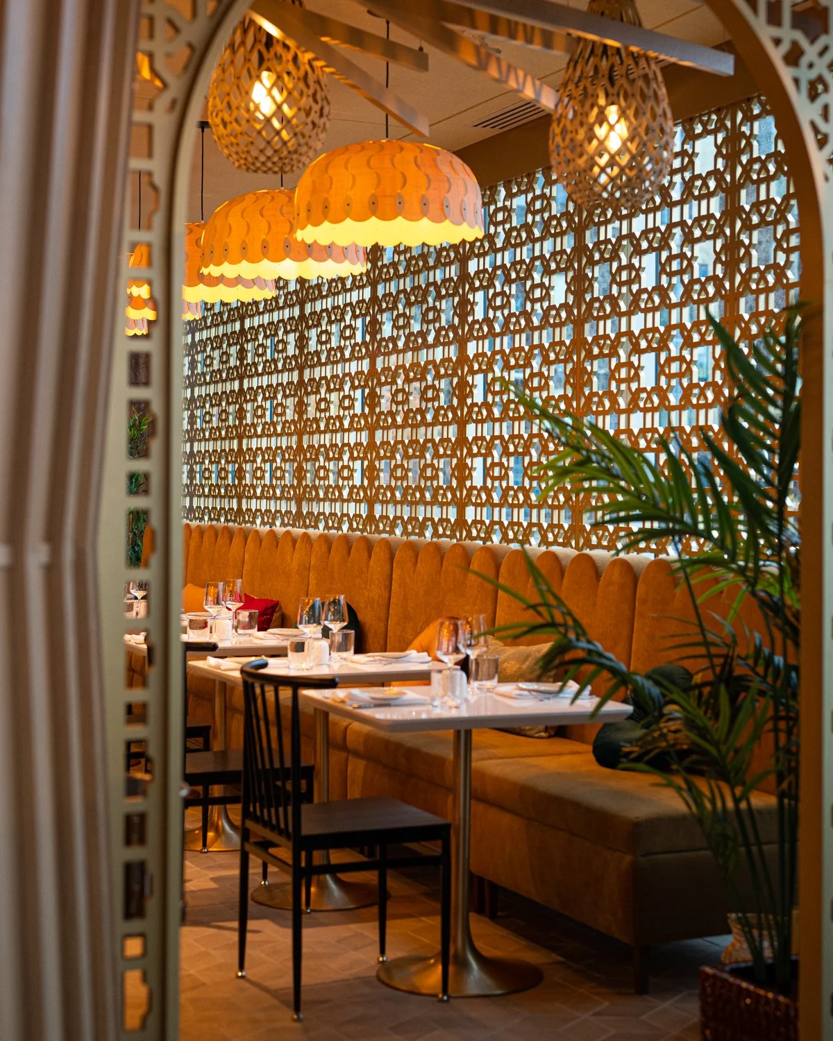 Warm wood restaurant interior with large yellow scalloped banquette, lattice screen and overhead lantern lights