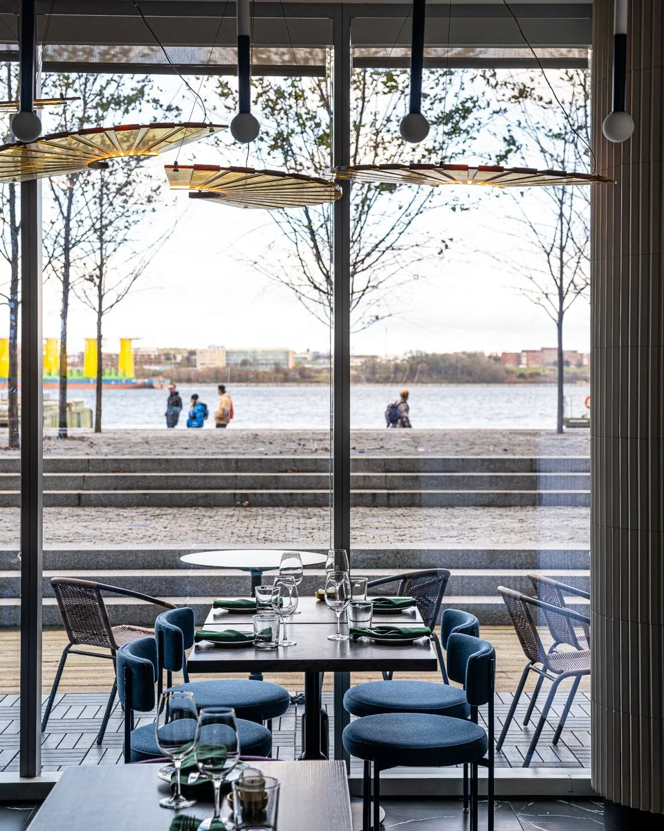 Restaurant interior with blue chairs at wood tables near large windows overlooking Halifax Harbour