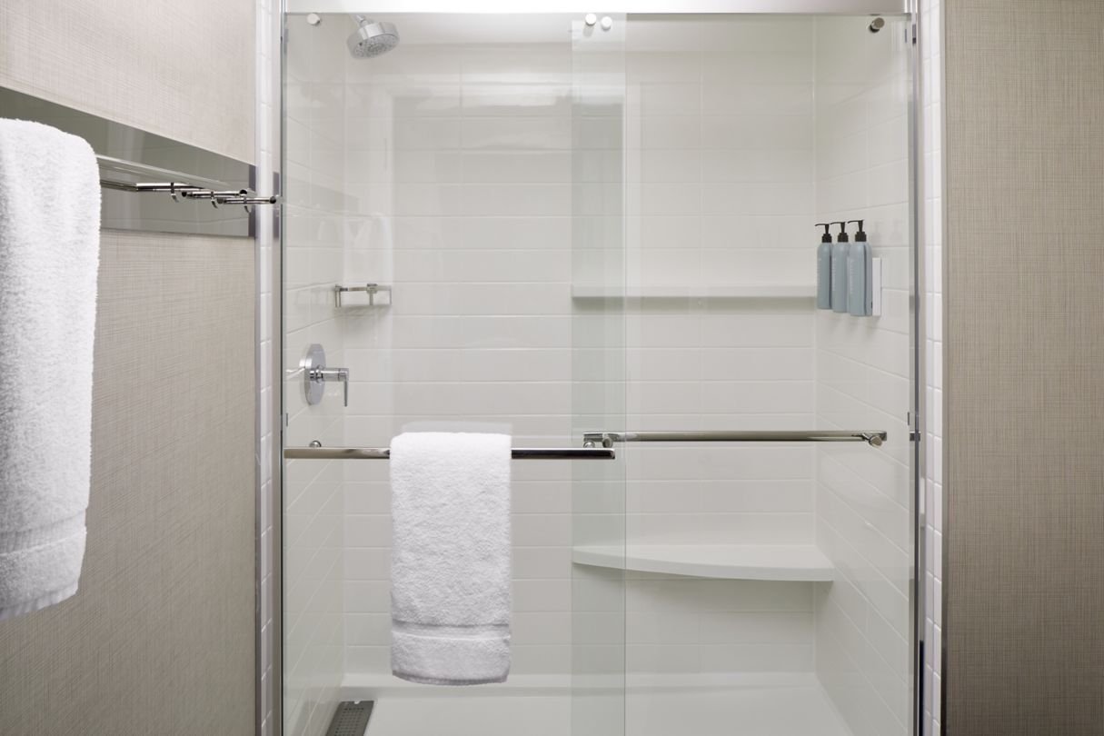 Hotel guestbath walk-in shower with ledge, robe hooks and glass doors