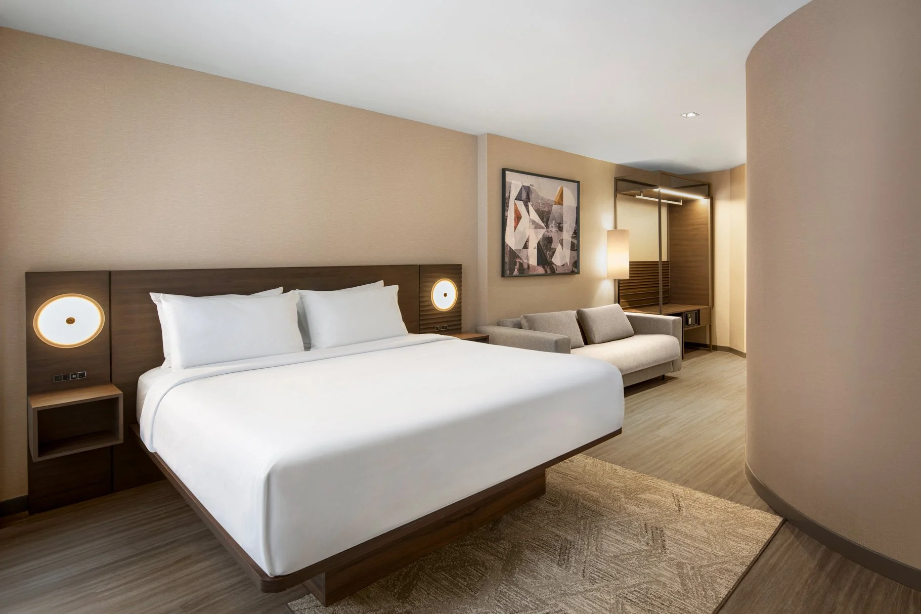 King hotel guestroom with wood bed, closet and upholstered sofa with artwork