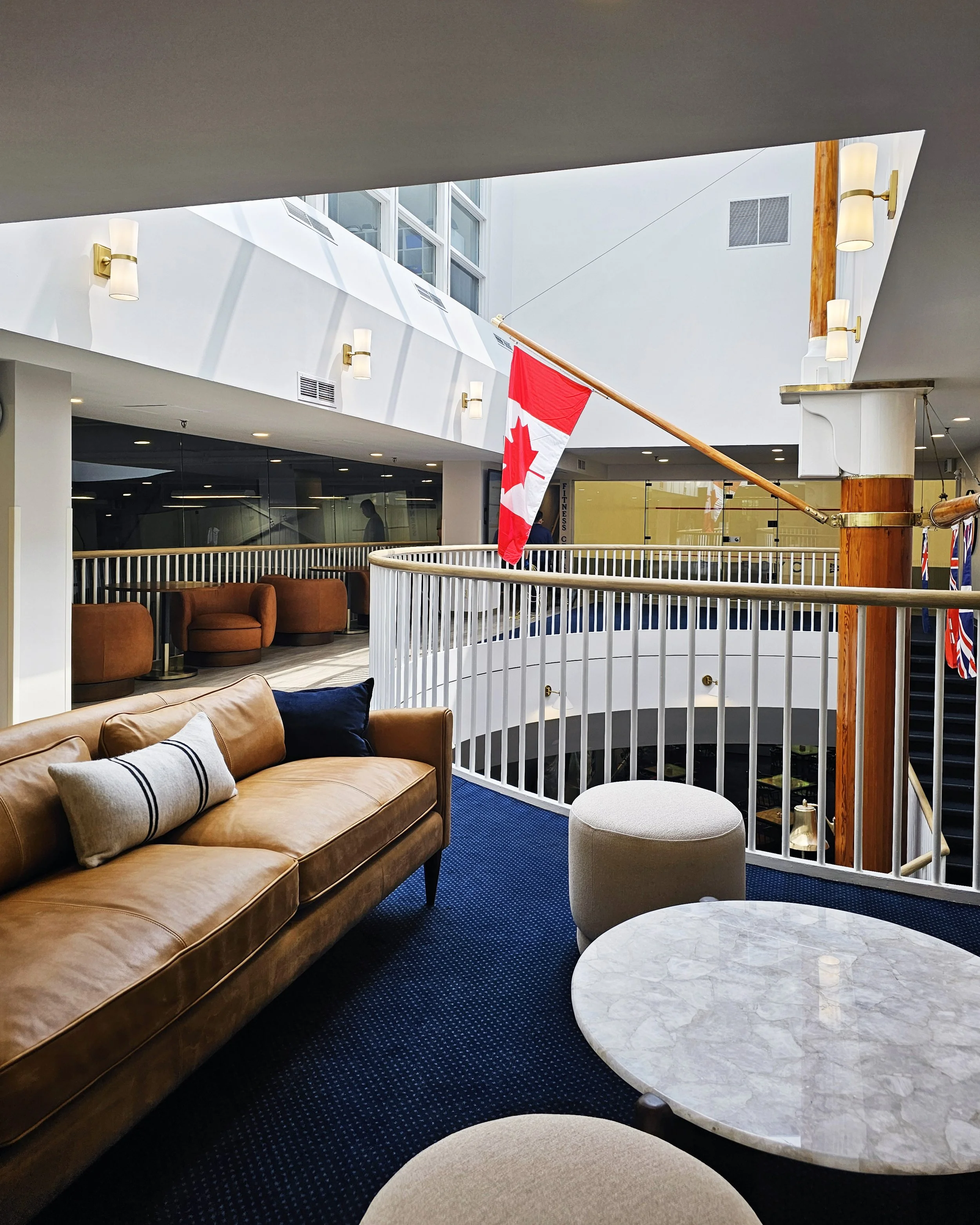Mezzanine lounge space with blue carpet, leather seating and accent tables near squash courts