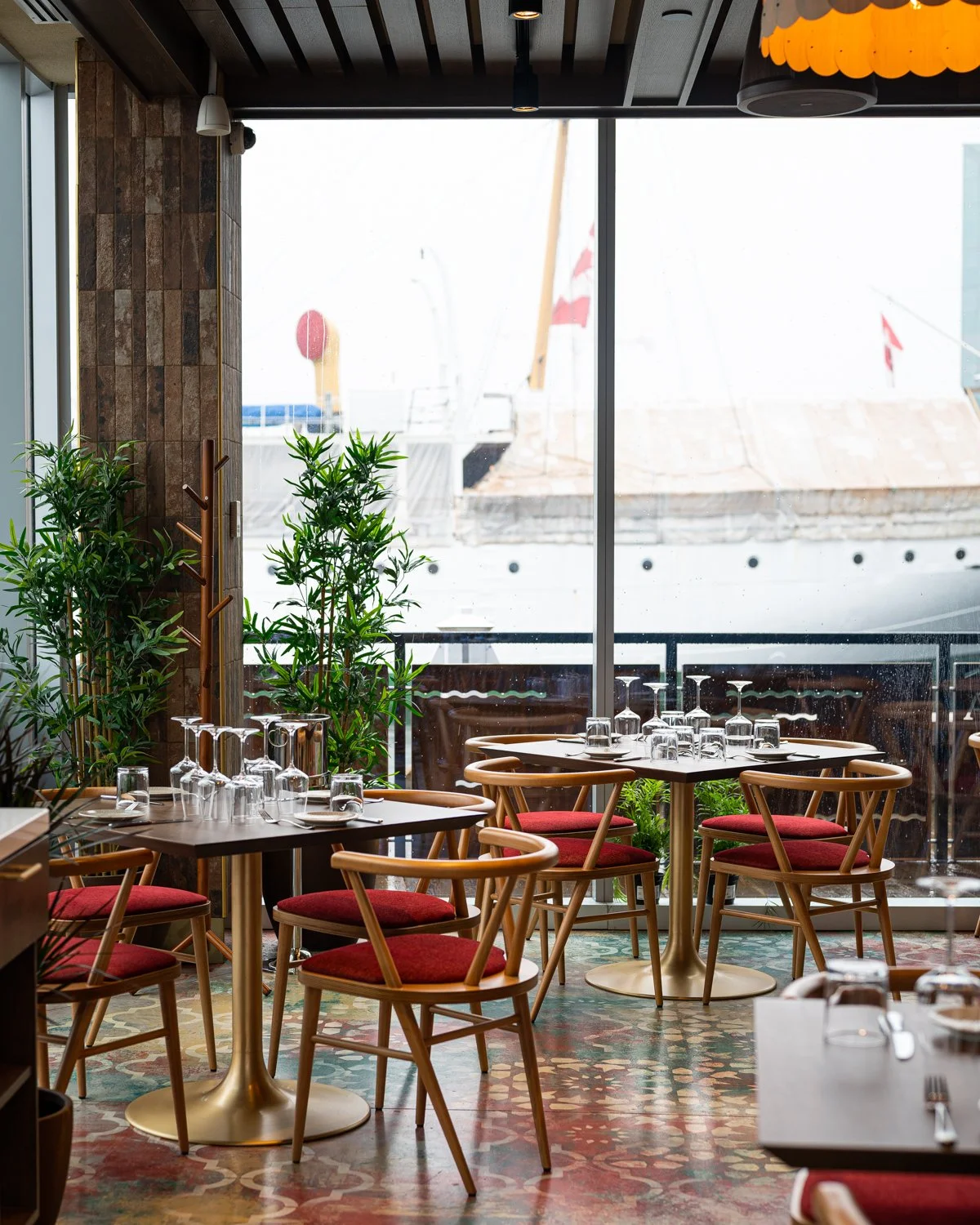 Restaurant interior with red cushioned chairs, patterned floor and large windows facing Halifax Harbour