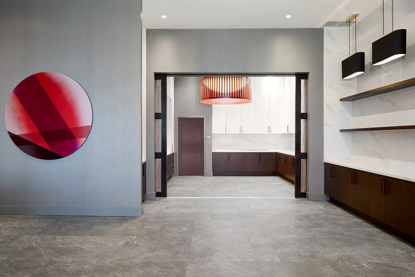 Buffet food service area with wood stained lower cabinets, quartz countertops, and white upper cabinets with accent black and red pendants