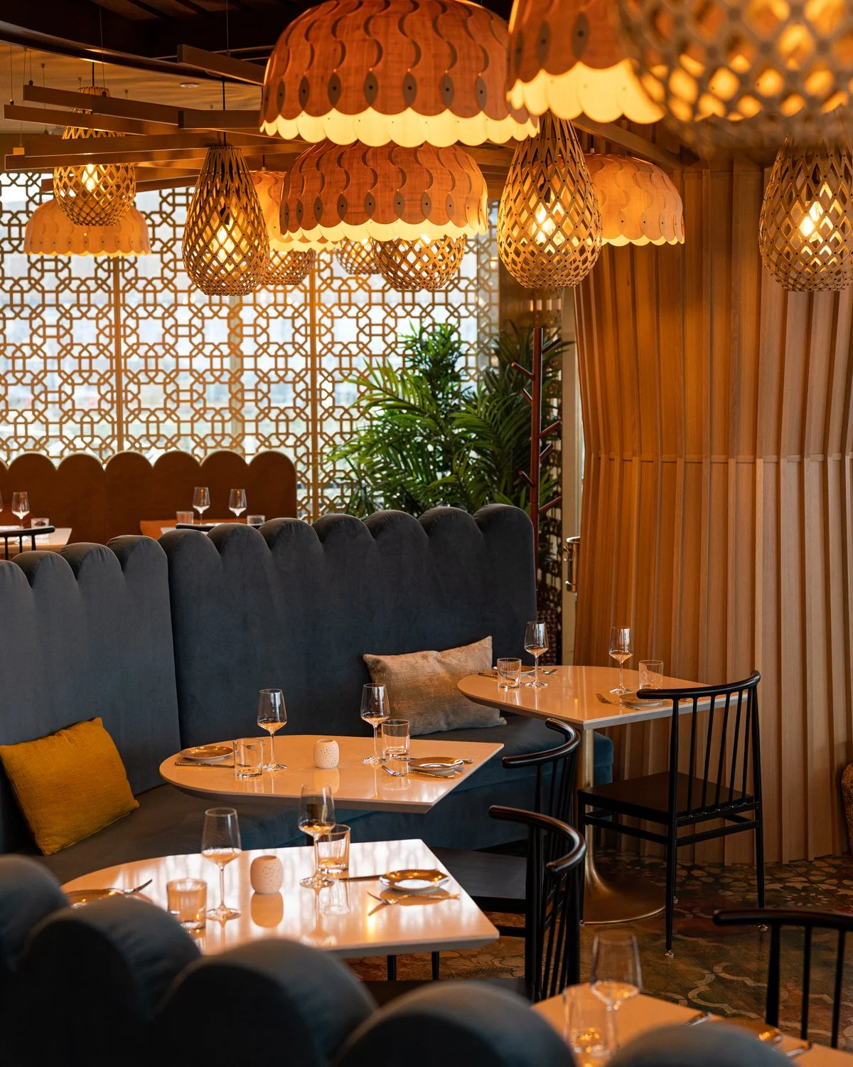 Warm wood restaurant interior with black wood chairs, large curving blue scalloped banquette and overhead lantern lights