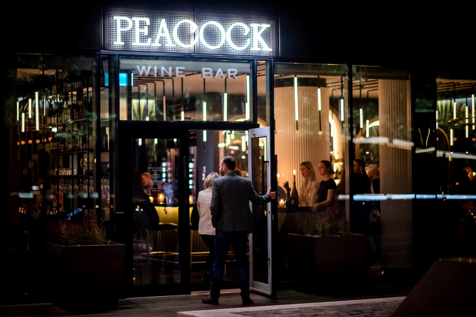 Night time image of restaurant exterior with signage over front door with guests arriving