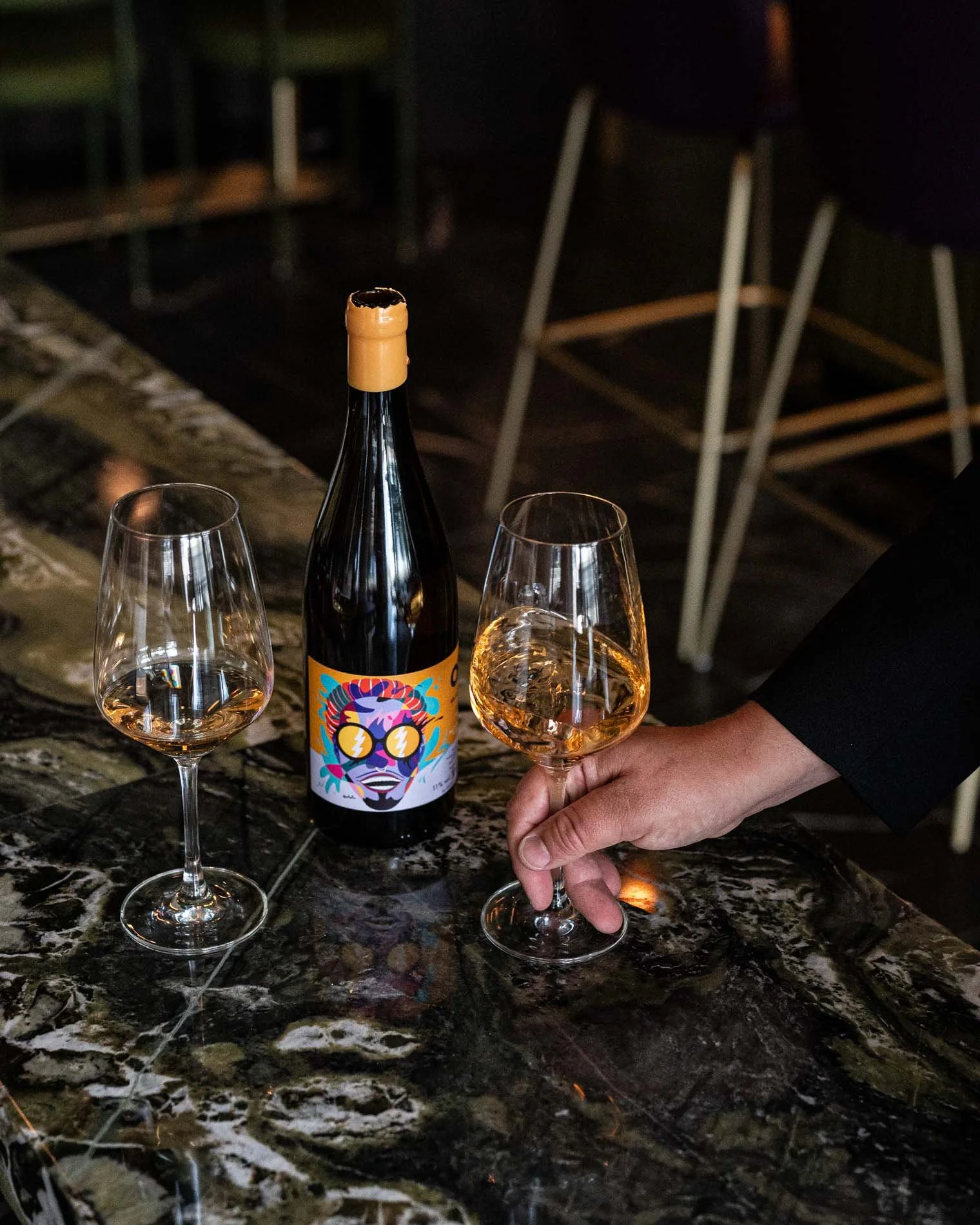 Close up shot of hand grabbing one of two wine glasses on green marble table
