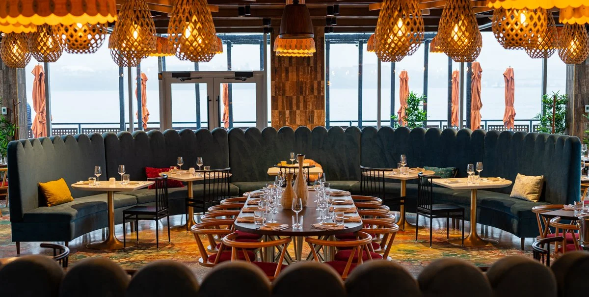 Warm wood restaurant interior with red cushioned chairs, large curving blue scalloped banquette and overhead lantern lights