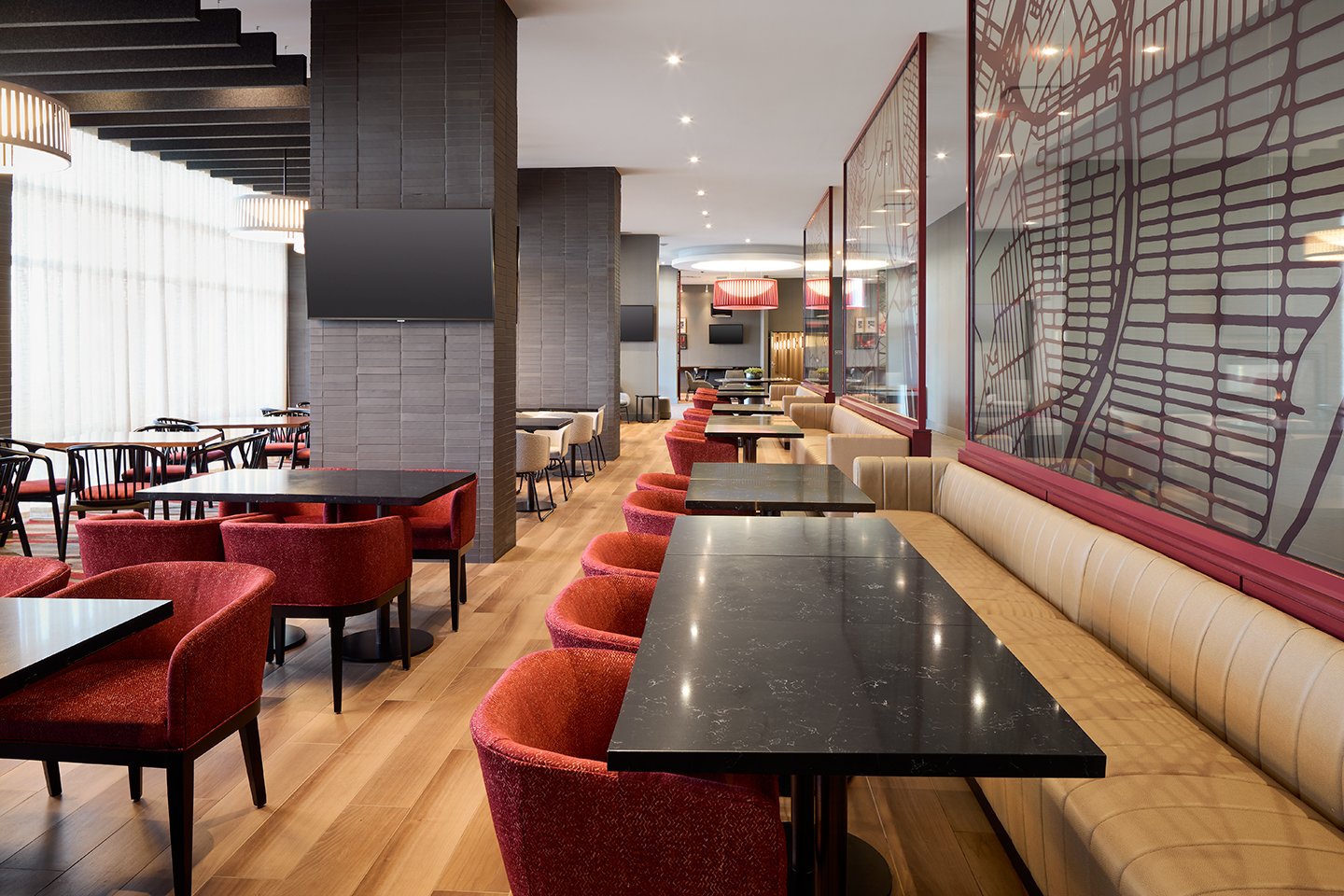 Hotel restaurant with red fabric seating, leather banquettes, quartz top tables, with red decorative aerial map screens and grey stone walls