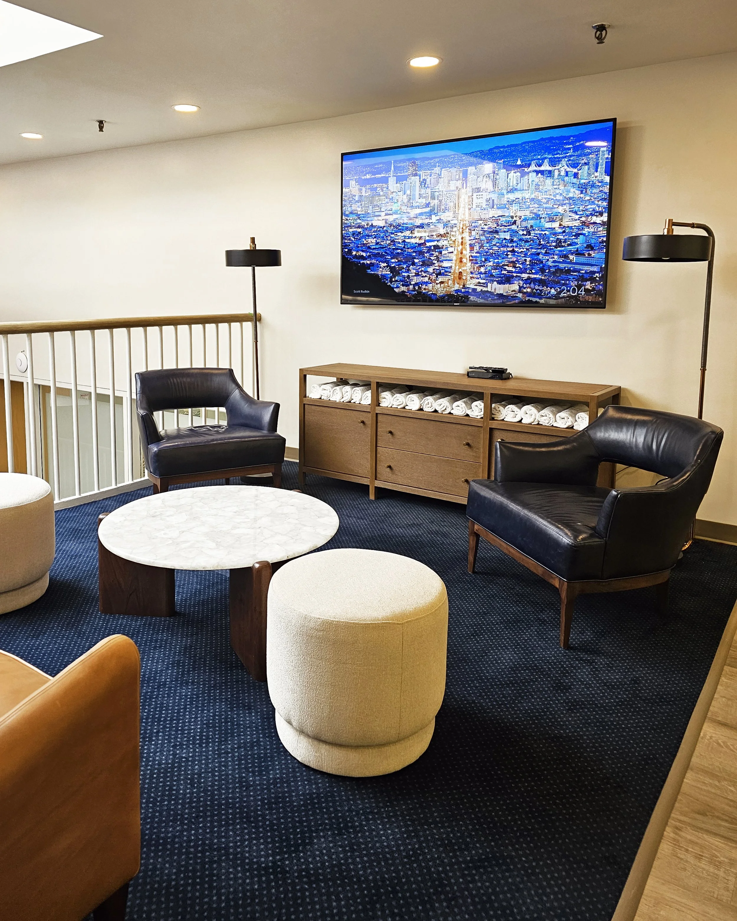 Mezzanine lounge space with blue carpet, leather seating and accent tables with TV and amenity console