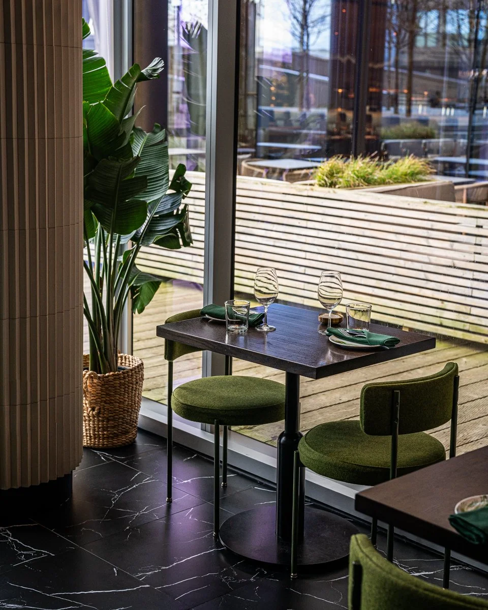 Restaurant interior with green chairs at wood table near large windows with black marble floor tile