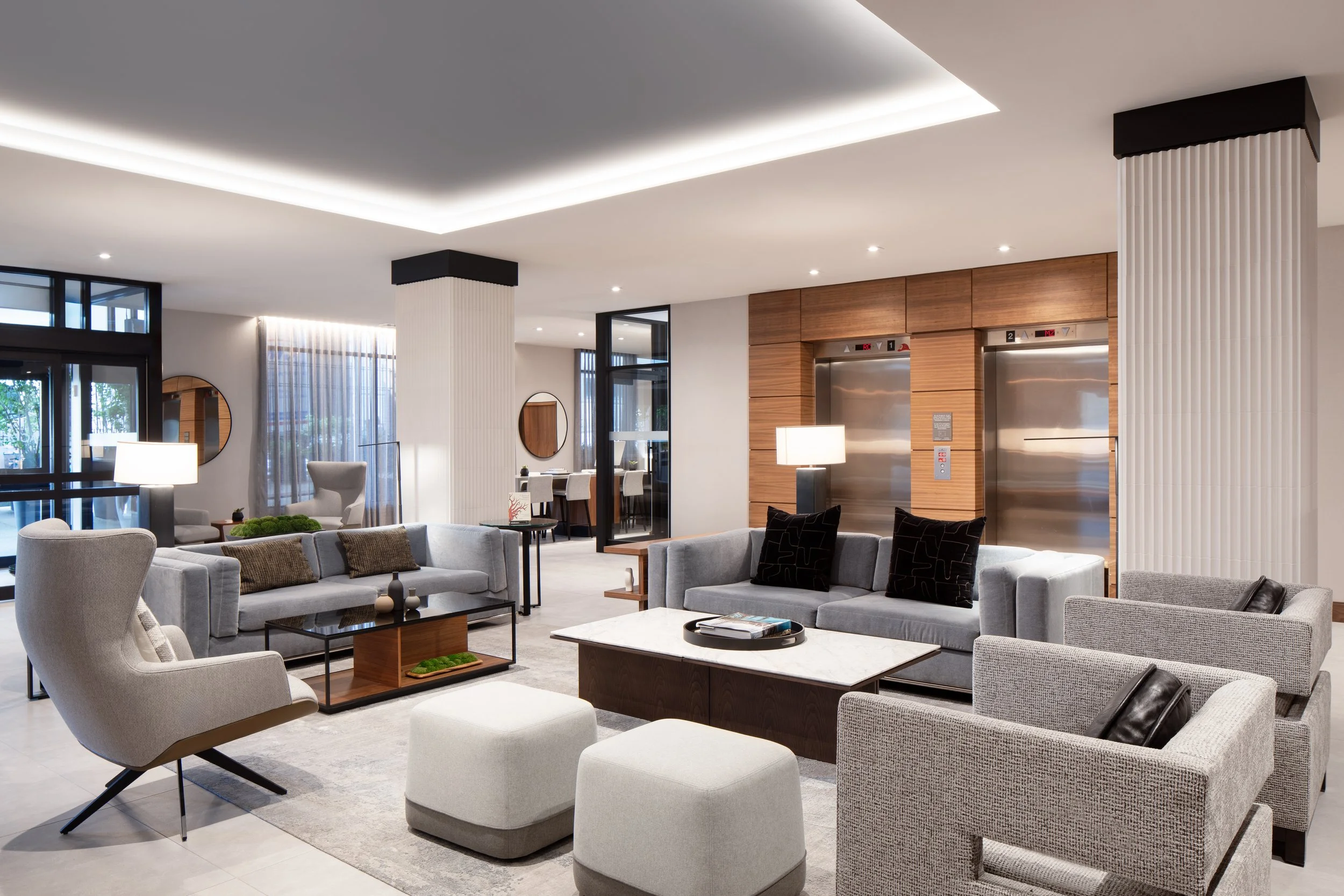 Large seating area with fabric sofas and chairs surrounded by architectural columns and elevators