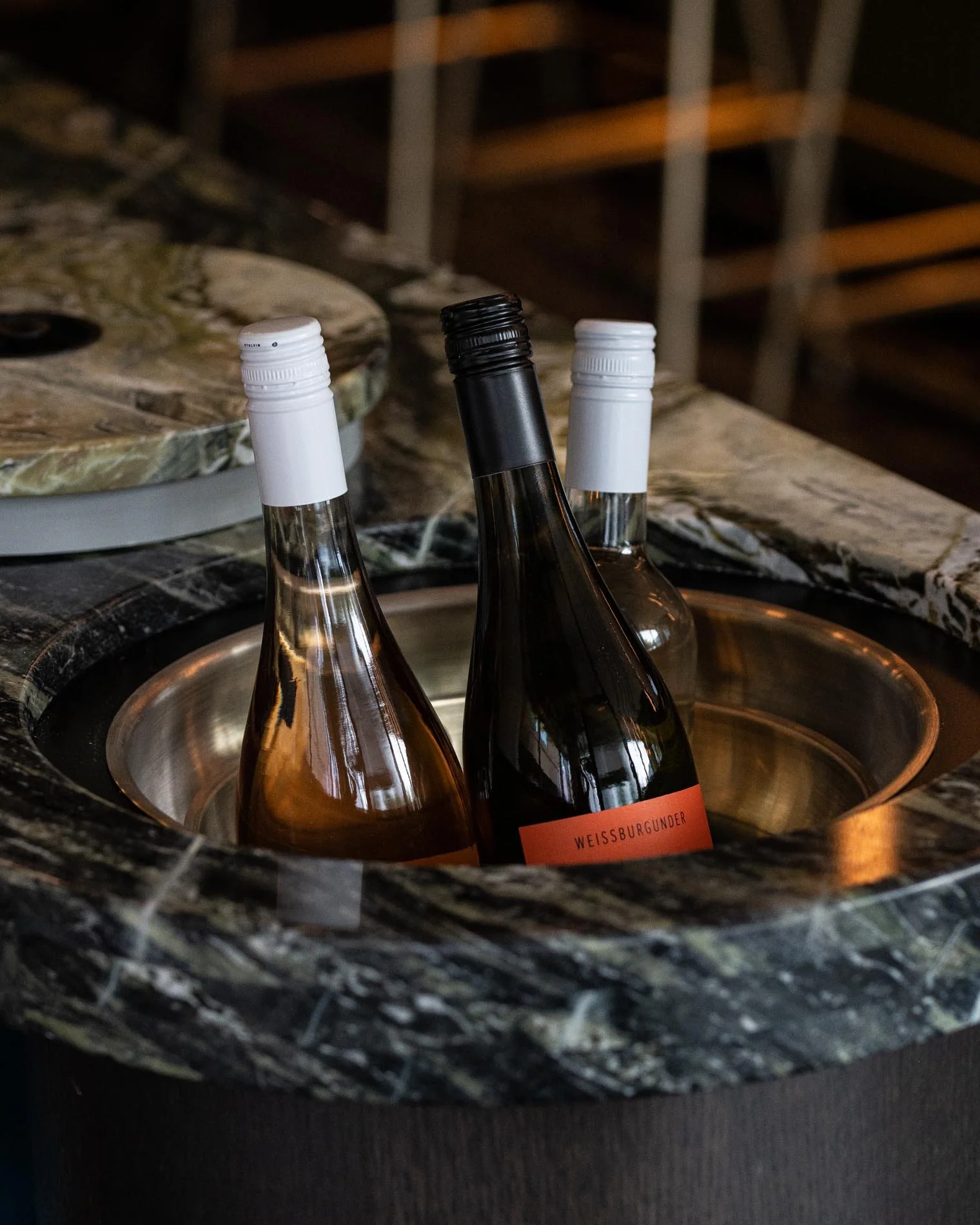 3 bottles of wine sitting in ice bucket integrated into table with green veined marble