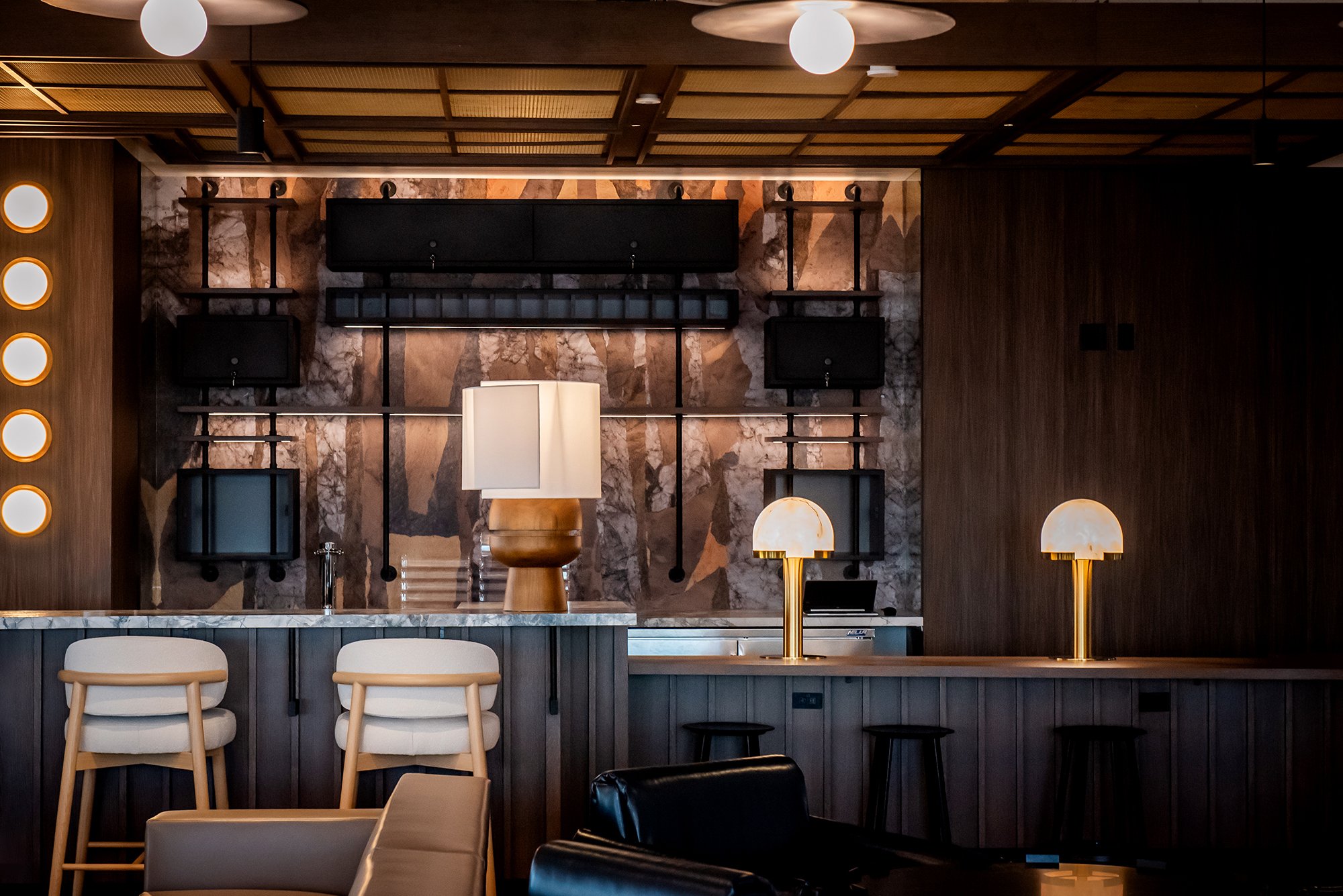 Large wood and stone bar with upholstered stools and warm lighting
