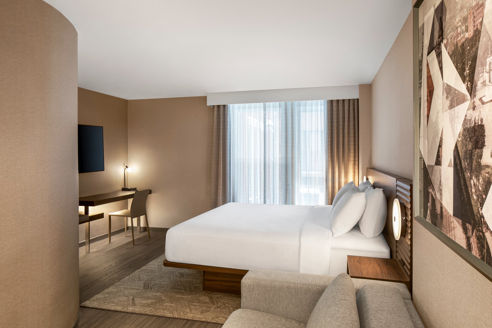 King hotel guestroom with wood bed, desk and upholstered sofa