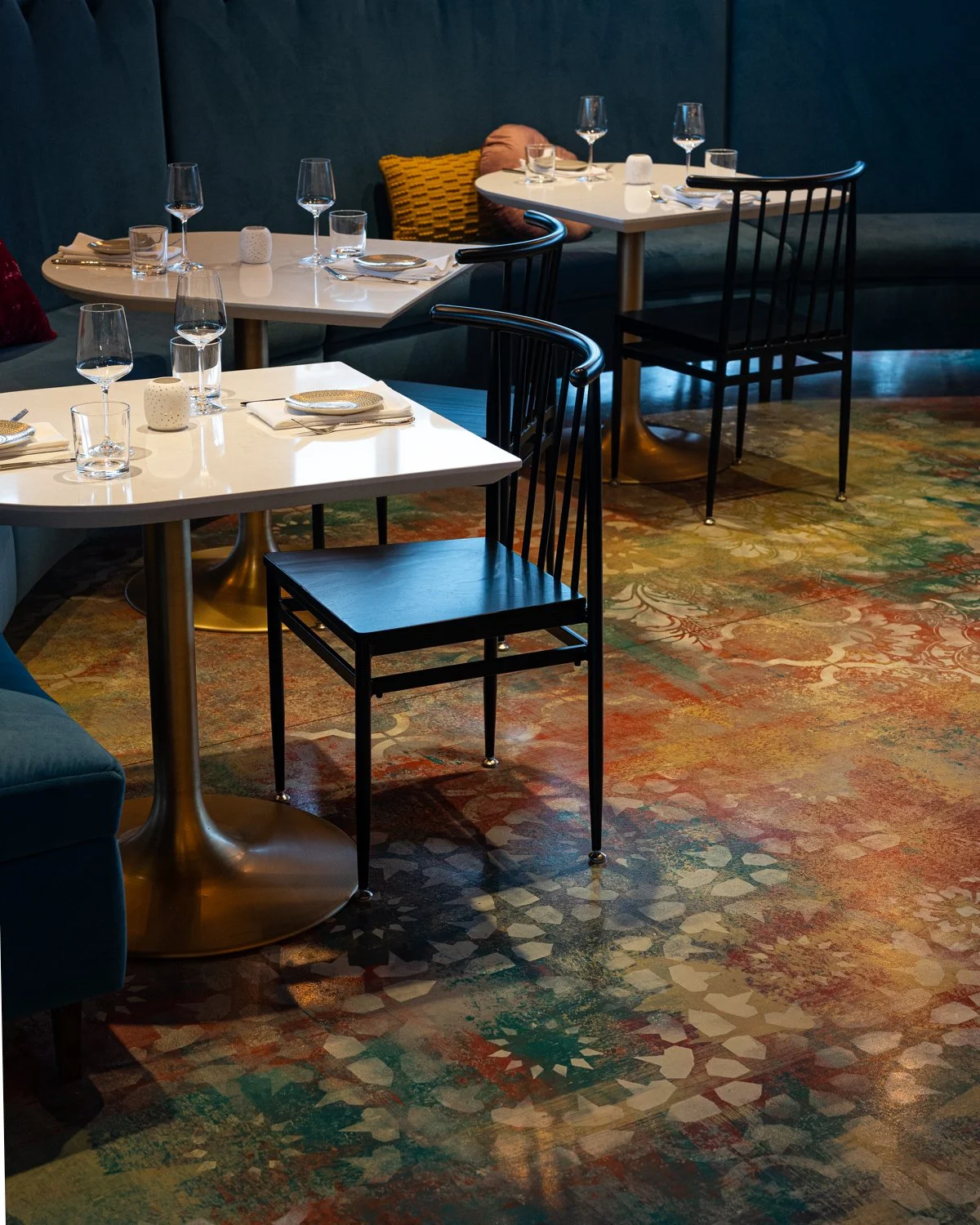 Restaurant interior with black wood chairs, large curving blue banquette and patterned floor