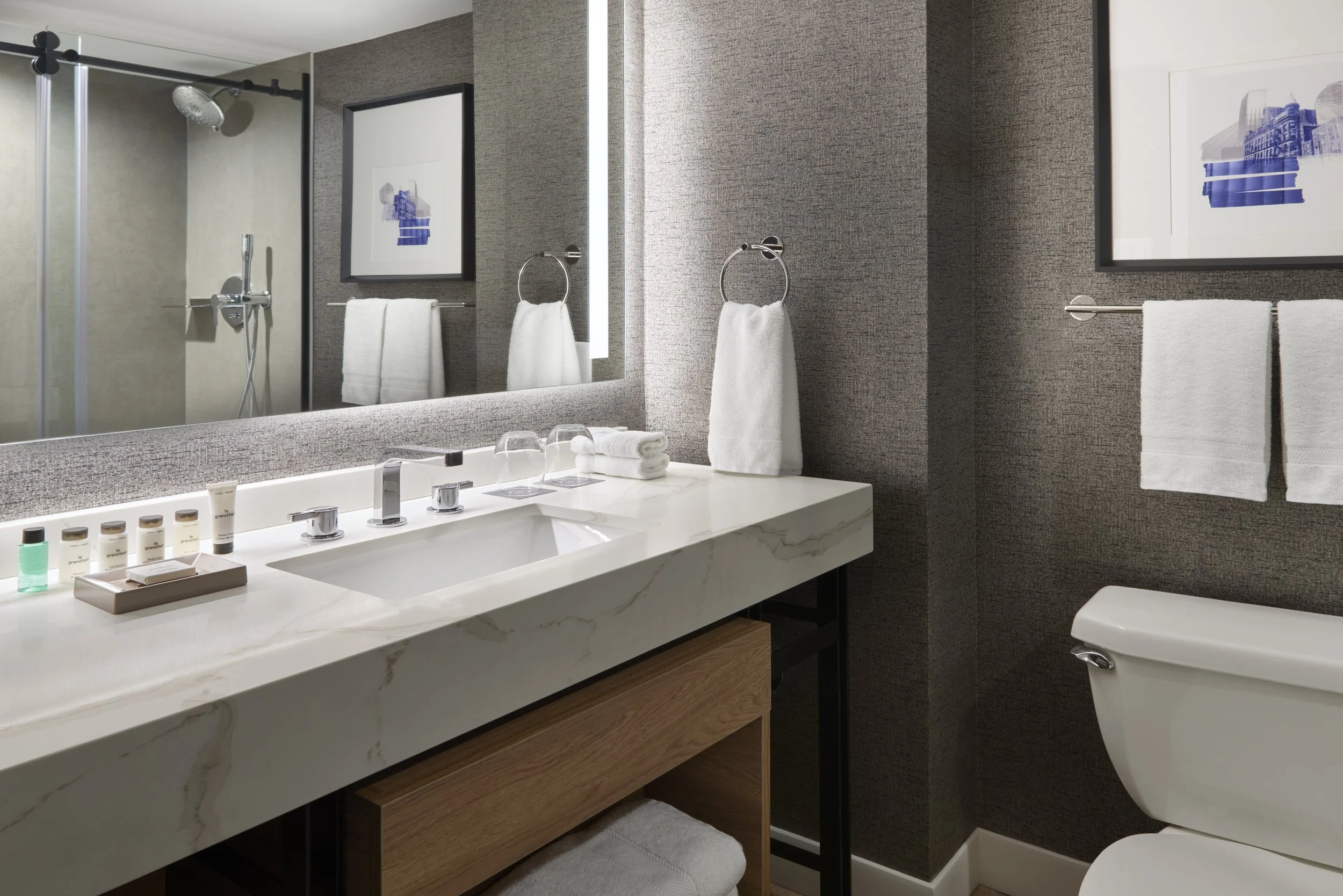 Hotel guest bath with dark wallcovering, wood vanity and large shower