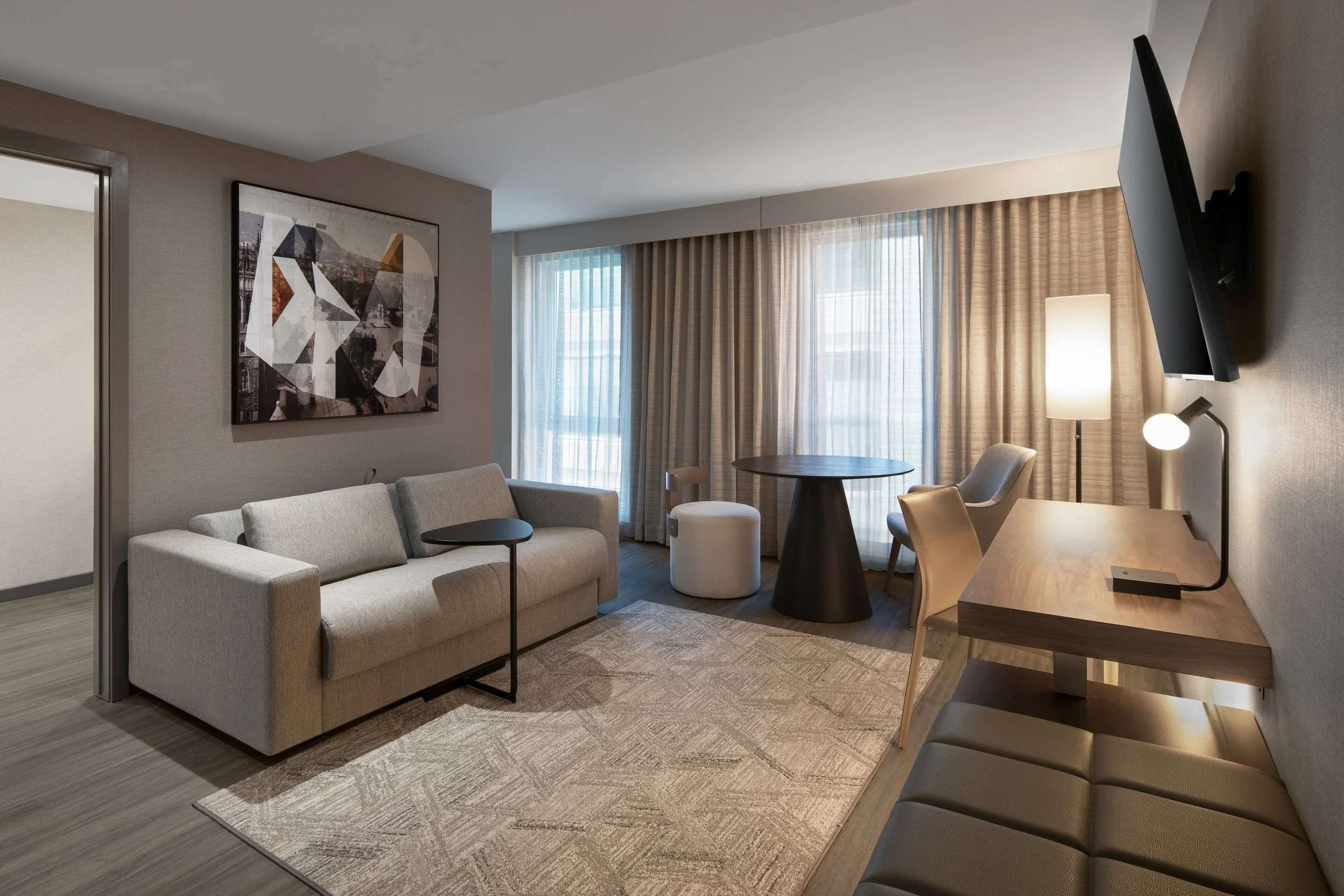 Hotel guestroom with upholstered sofa with artwork, desk, and dining table