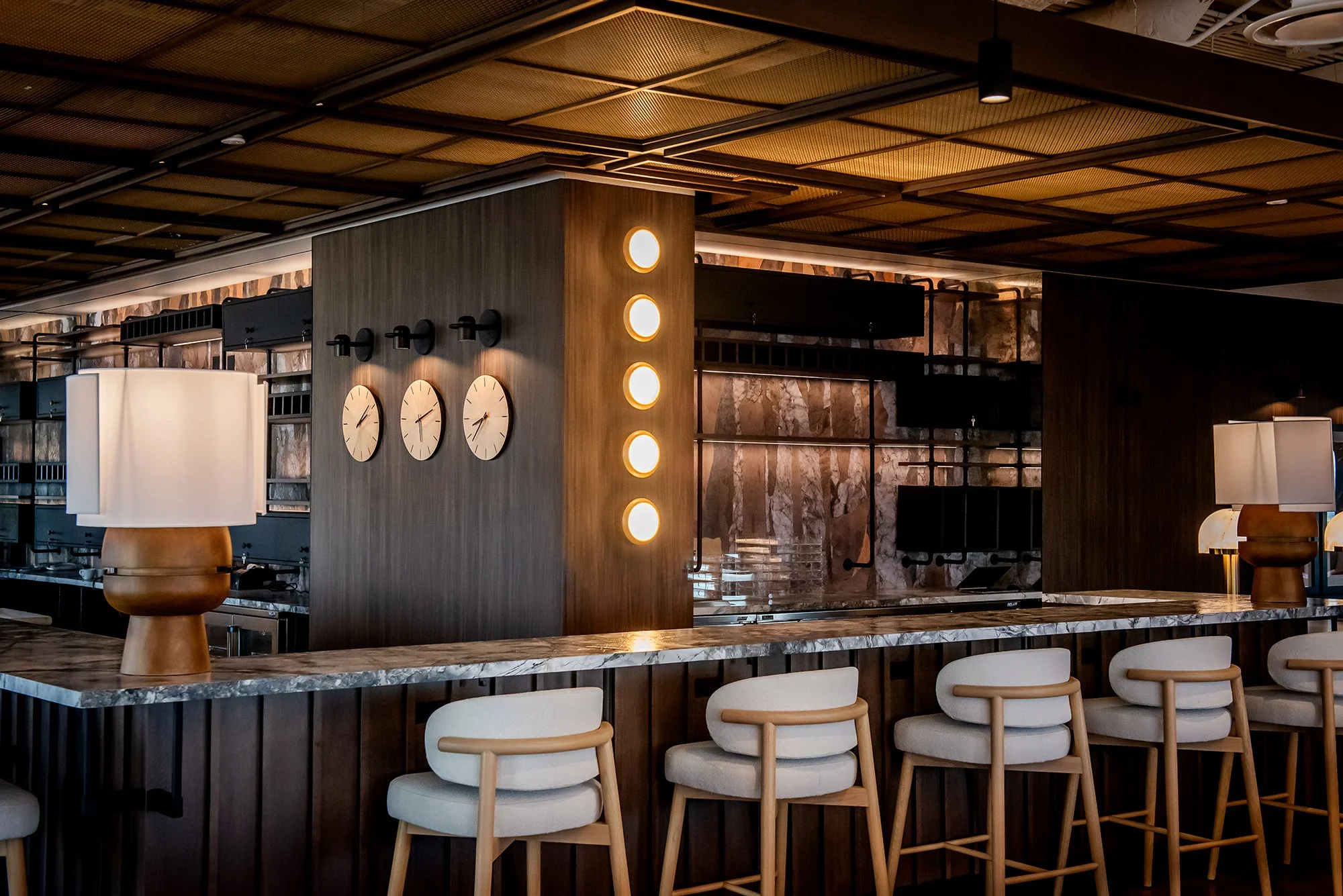Large wood and stone bar with upholstered stools and warm lighting