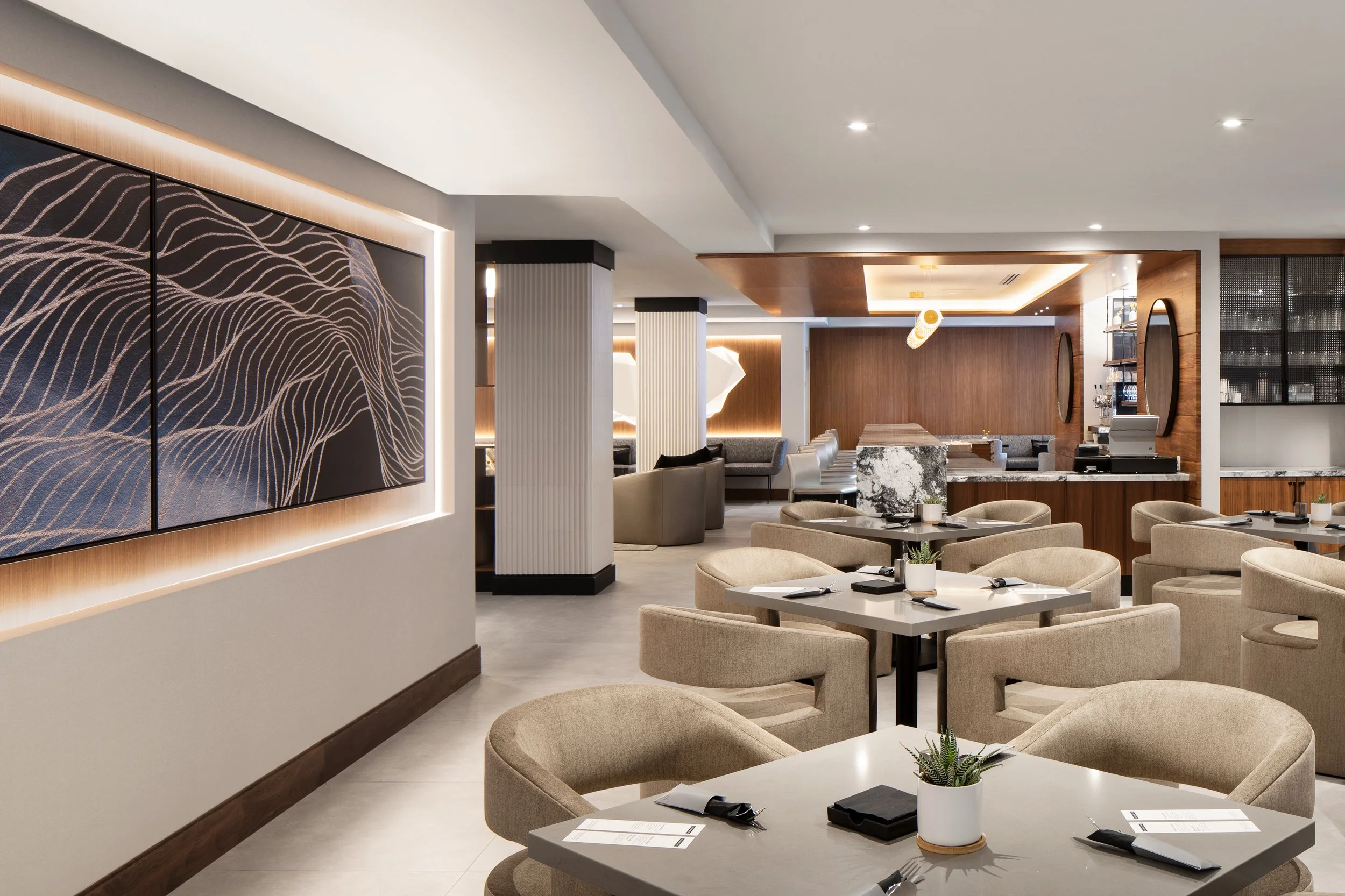 Open concept restaurant with upholstered seating, large artwork and expansive wood and stone bar