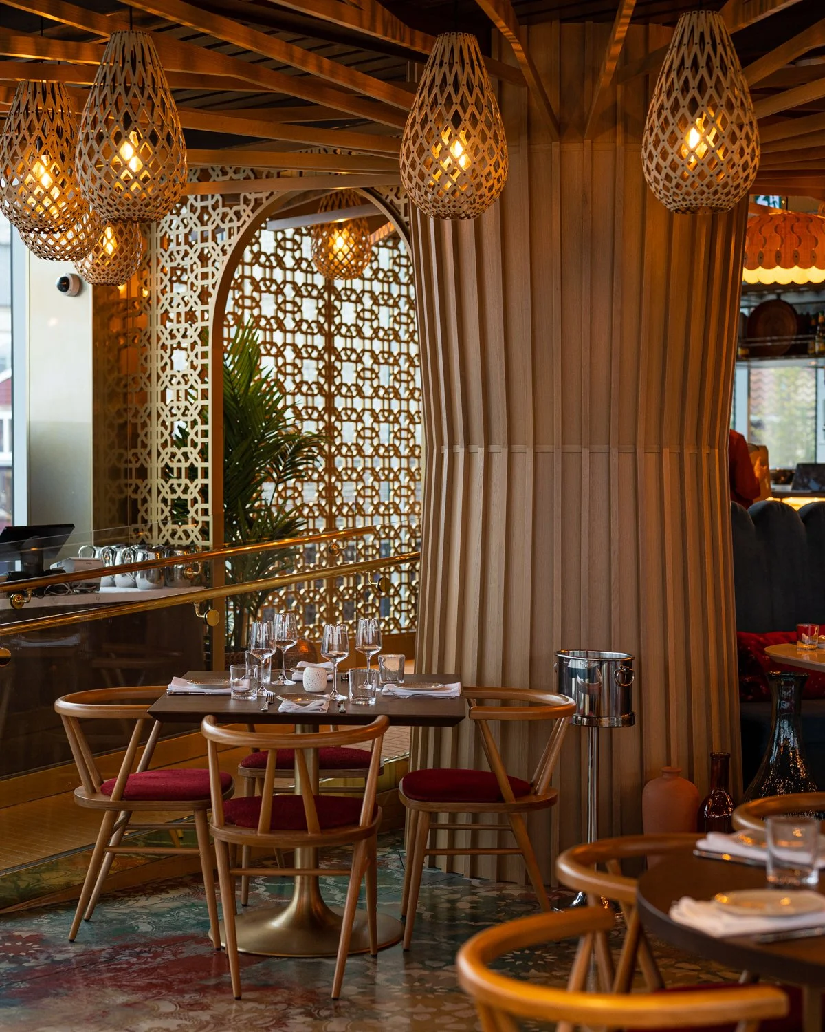 Warm wood restaurant interior with red cushioned chairs, lattice screen and overhead lantern lights