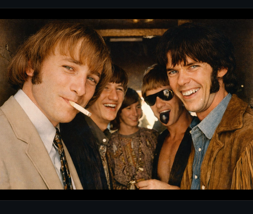 Group of five friends smiling at a social gathering, with one smoking a cigarette.