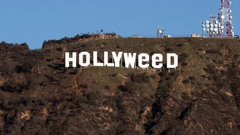 The Hollywood sign on a hillside with TV antennas and satellite dishes at the top, under a clear blue sky.