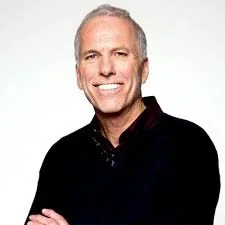 A smiling middle-aged man with short gray hair, wearing a black shirt, against a plain white background.