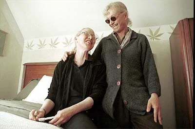 Two women, one elderly and one younger, sharing a joyful moment in a room, sitting on a bed and smiling.