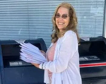 Woman holding a large stack of papers, standing next to a copier or printer machine, smiling, in an office or workplace setting.