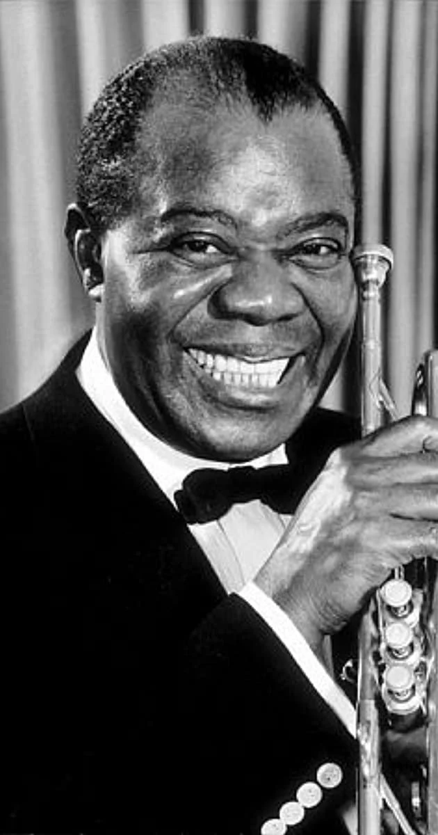 Black and white photo of a smiling man in a tuxedo holding a saxophone.