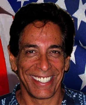A man with dark hair smiling in front of American flag-themed background.