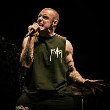 Male singer performing with microphone on stage, wearing a sleeveless green shirt.