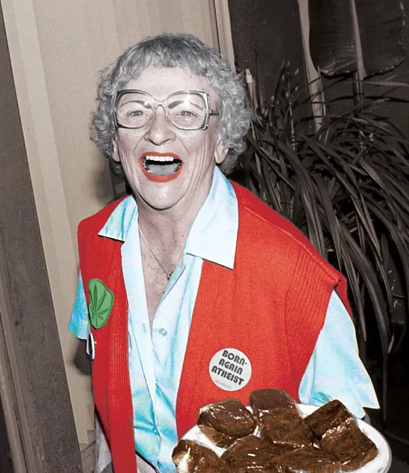 A person dressed as a grocery store cashier, wearing glasses, an orange vest, and a 'Born-Again Atheist' button, smiling and holding a plate of brownies.