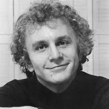 A black-and-white portrait of a young man with curly hair smiling at the camera.