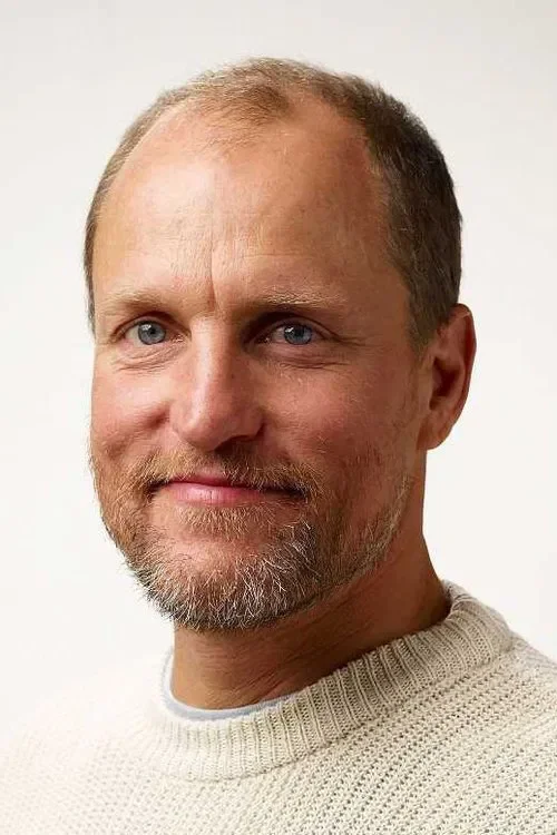 A middle-aged man with light skin, short light brown hair, a scruffy beard, and blue eyes, wearing a cream-colored knit sweater, smiling gently against a plain white background.