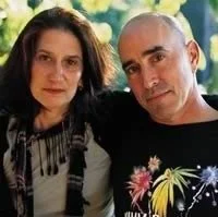A woman and a man pose together outdoors with greenery in the background.