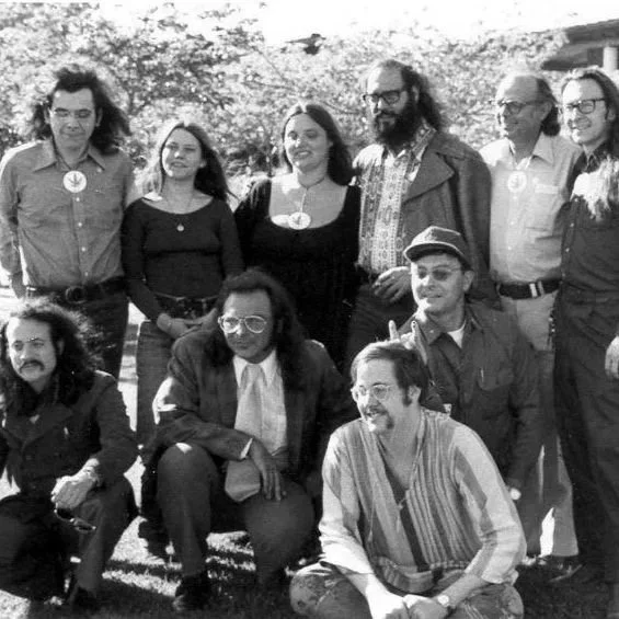 Group of nine people outdoors, some standing and some sitting, in black and white.