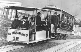 Vintage black and white photo of a small railroad tram with passengers, labeled 'Curi Shell Railroad Co., 18', on a track with a city street in the background.