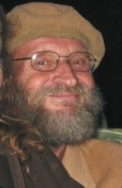 A man with a gray beard, glasses, and a tan hat smiling.