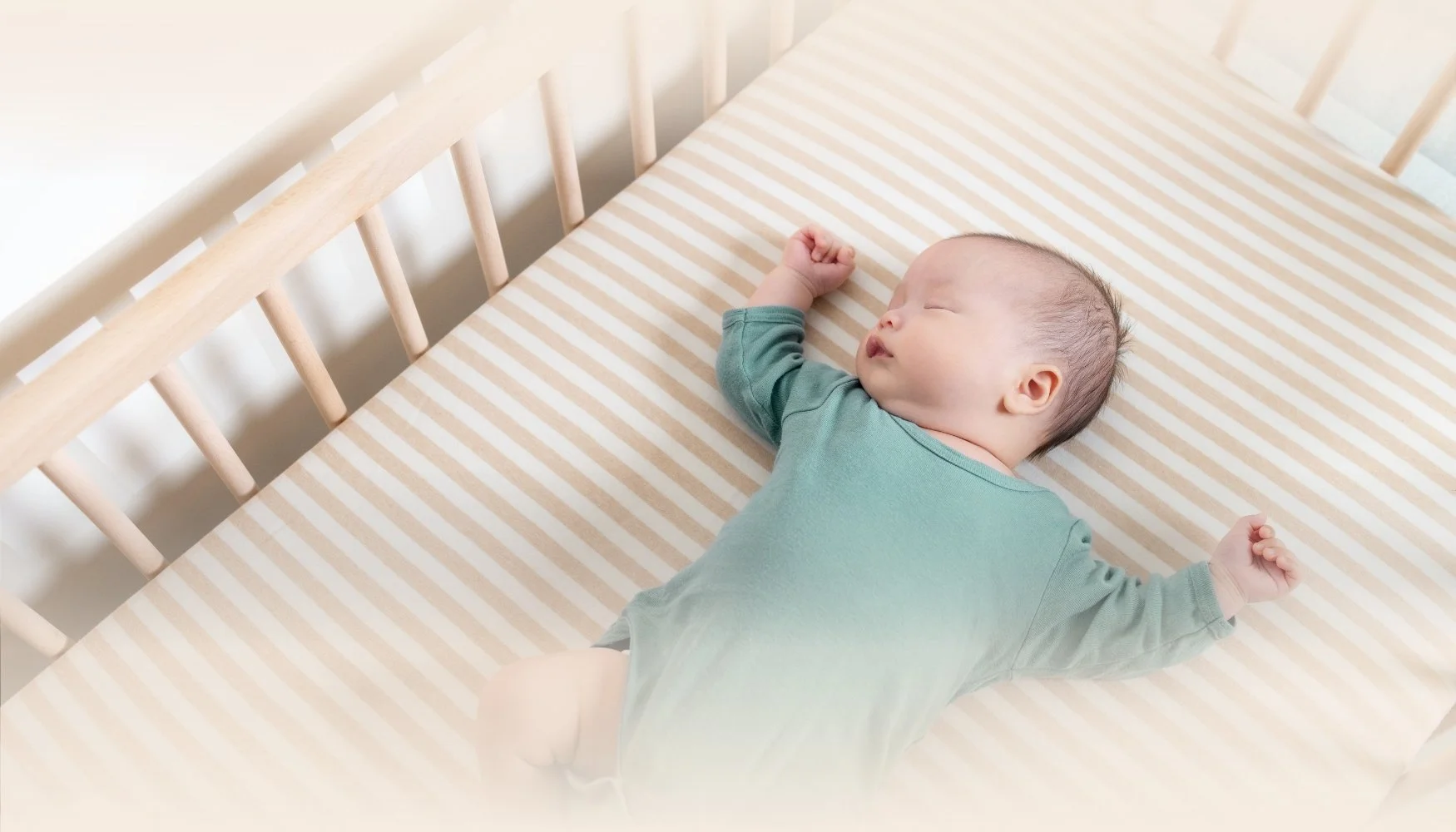 A baby sleeping in a wooden crib with beige and white striped bedding, wearing a green outfit.