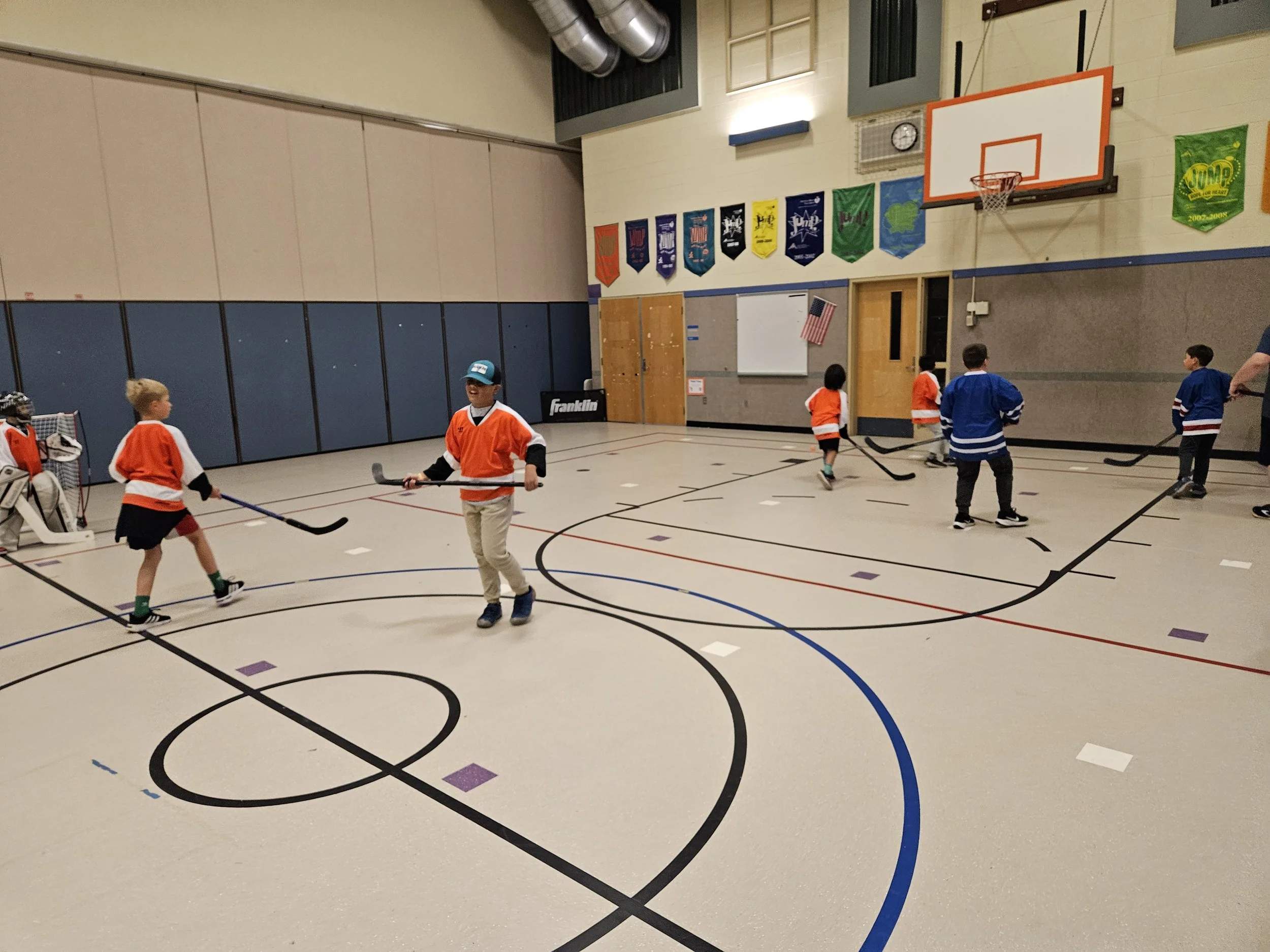 Children playing hockey in an indoor gymnasium.
