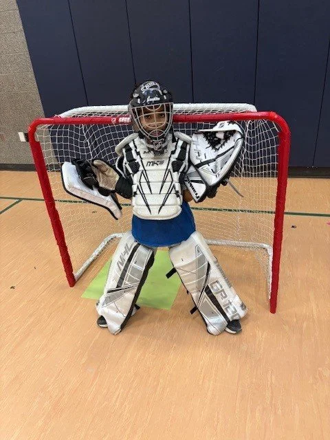 Youth ice hockey goalie in full gear standing in front of a small hockey net indoors.