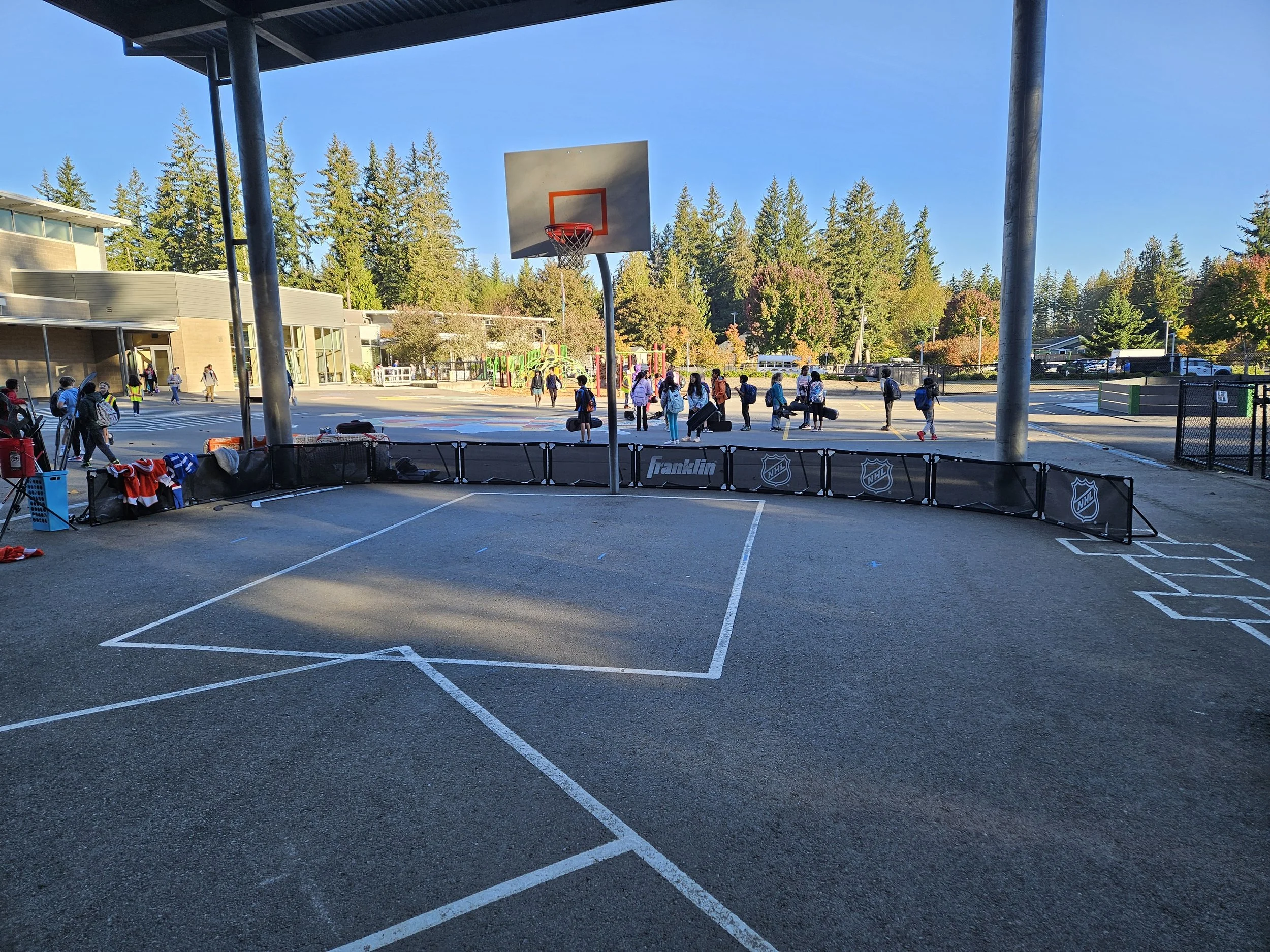 School students walking across a gymnasium courtyard with a basketball hoop, trees and a school building in the background.