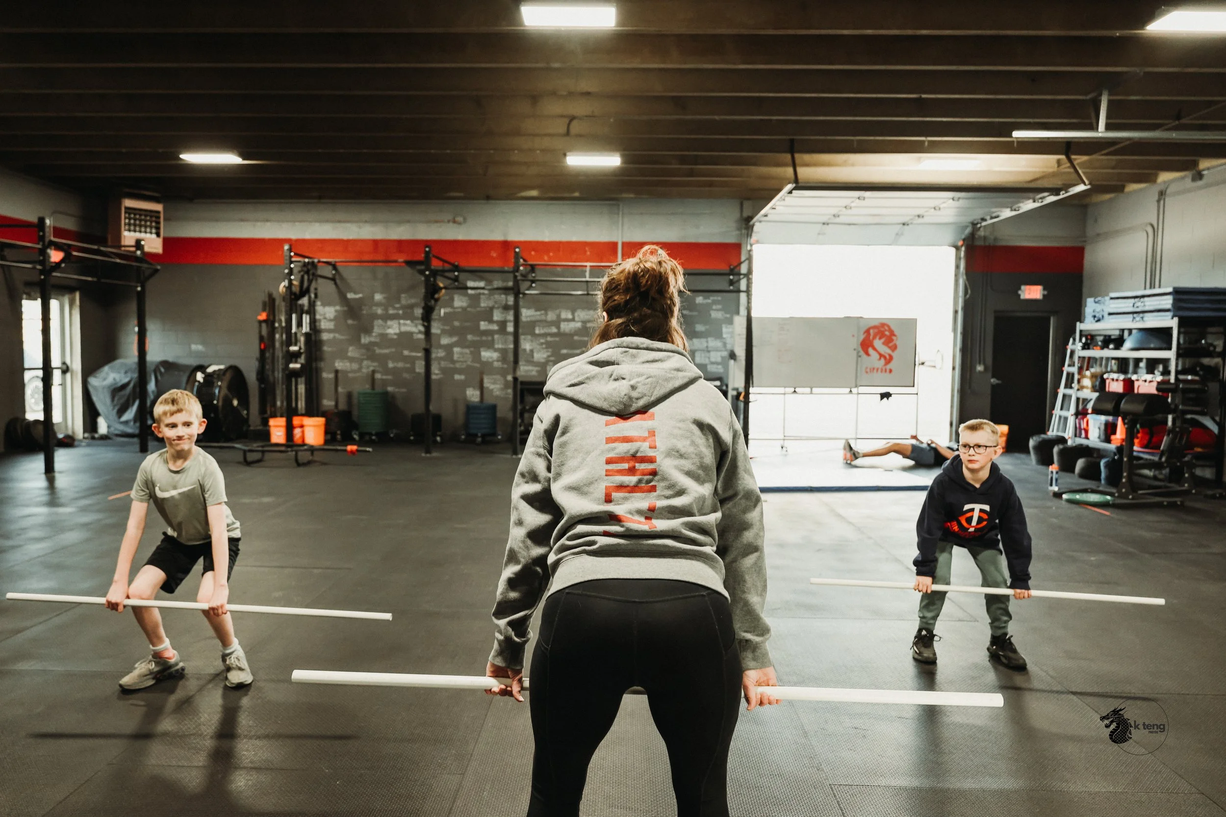 Coach Missy and two Pre-Teen Boys hold the hang position of a clean with PVCs.