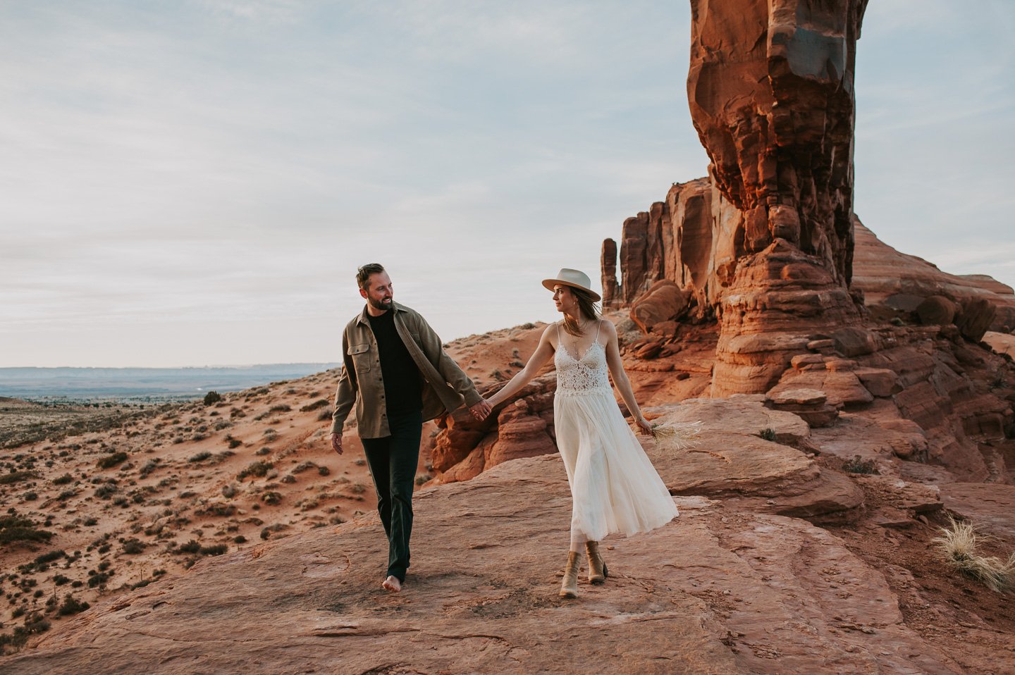 Couple walking hand in hand on red desert rocks under a blue sky while they elope in Utah near Canyonlands National Park.
