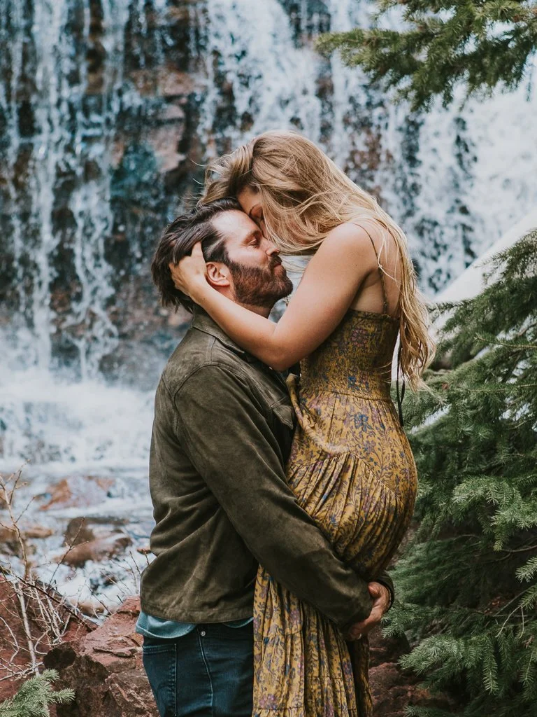 A couple embraces in the San Juan Mountains in front of a waterfall.