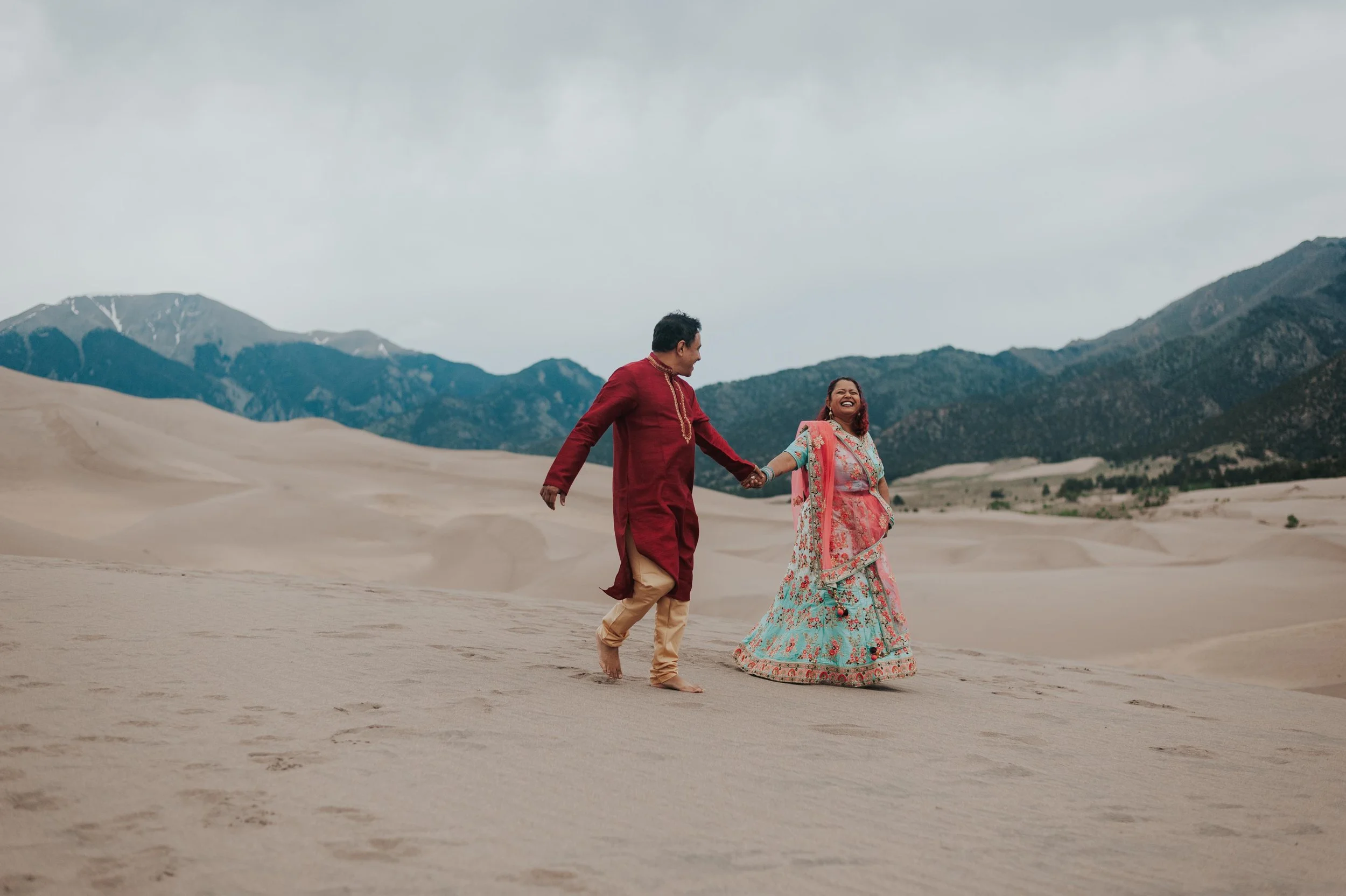 Indian couple running down the dunes holding hands at the Great Sand Dunes National Park.